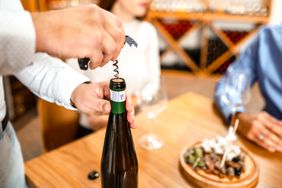 A sommelier opens a wine bottle for a young couple in a restaurant