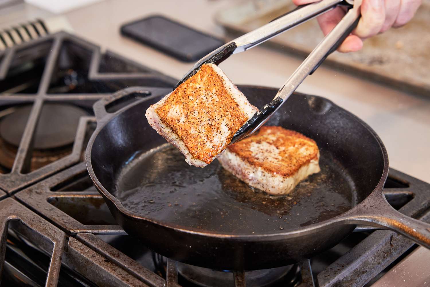 Hand using tongs to flip fish in Lodge Pre-Seasoned Cast Iron