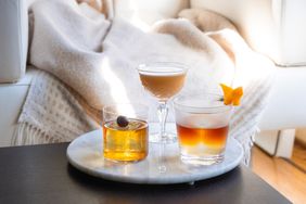 Three different cocktails on a tray sitting on a coffee table in front of a couch.