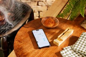 A phone with The Meater Plus Smart Meat Thermometer app displayed on a table next to a bowl of spice and the charger