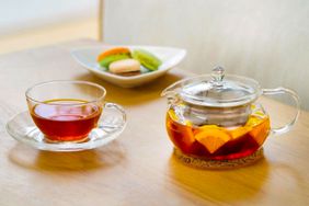 Teapots and a cup of citrus tea with a side of macroons.