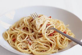 Close-up view of a serving of creamy spaghetti carbonara plated in a white bowl.