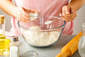 A person adds ingredients to a bowl of flour