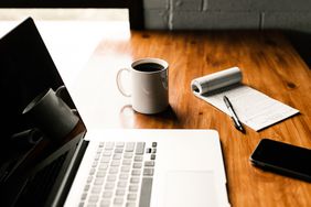 A desk set up for work with a laptop, notepad and coffee mug