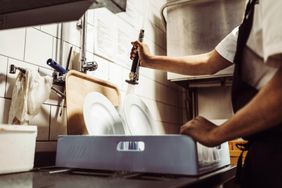 A porter cleans a crate of dishes in a restaurant kitchen