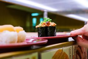 A person grabs a tray off a conveyor belt at a sushi restaurant