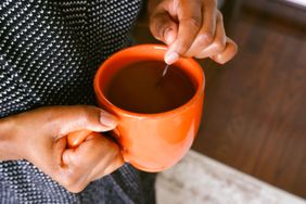 A person stirs coffee in a large orange mug